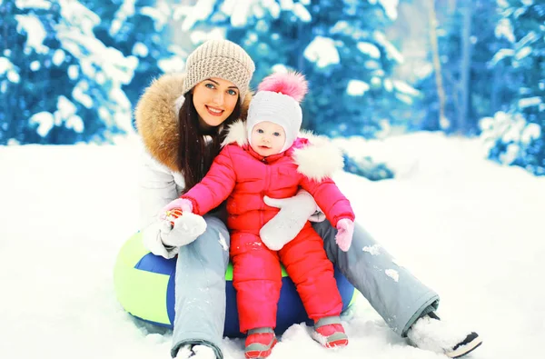 Winter gelukkig lacht moeder en kind zittend op een slee in besneeuwde d — Stockfoto