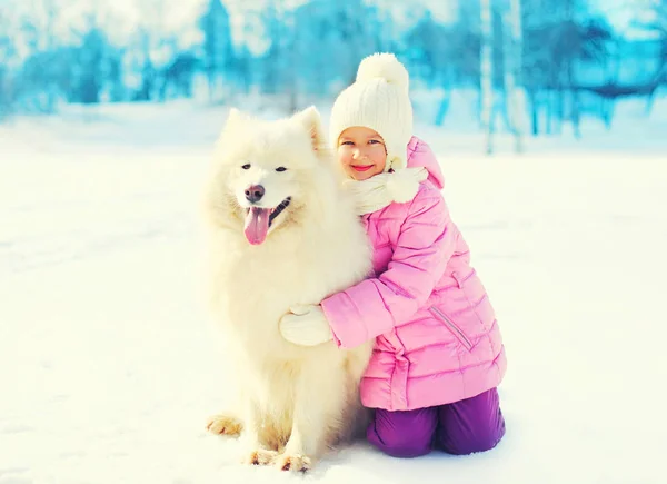 Happy smiling child embracing white Samoyed dog on snow winter — Stock Photo, Image