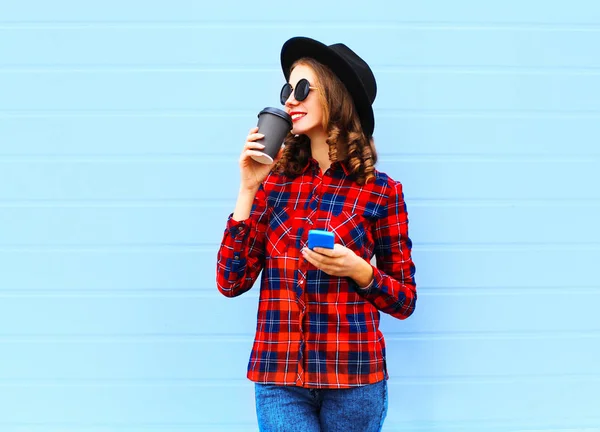 Модная молодая улыбающаяся женщина с чашкой кофе, смартфоном на улице — стоковое фото