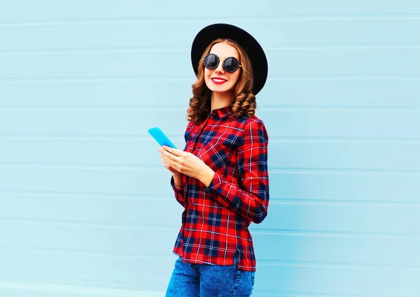 时尚的年轻女子使用智能手机的 n 市，认为戴一顶黑色的帽子 — 图库照片
