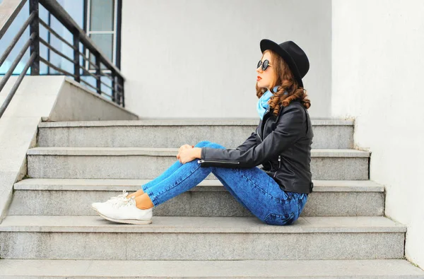 Fashion pretty young woman wearing black rock jacket, hat in cit