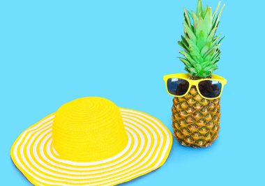 Ananas ile güneş gözlüğü ve sarı saman plaj şapka mavi bac üzerinde