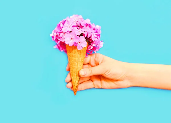 Tangan memegang es krim kerucut dengan bunga di atas latar belakang biru — Stok Foto