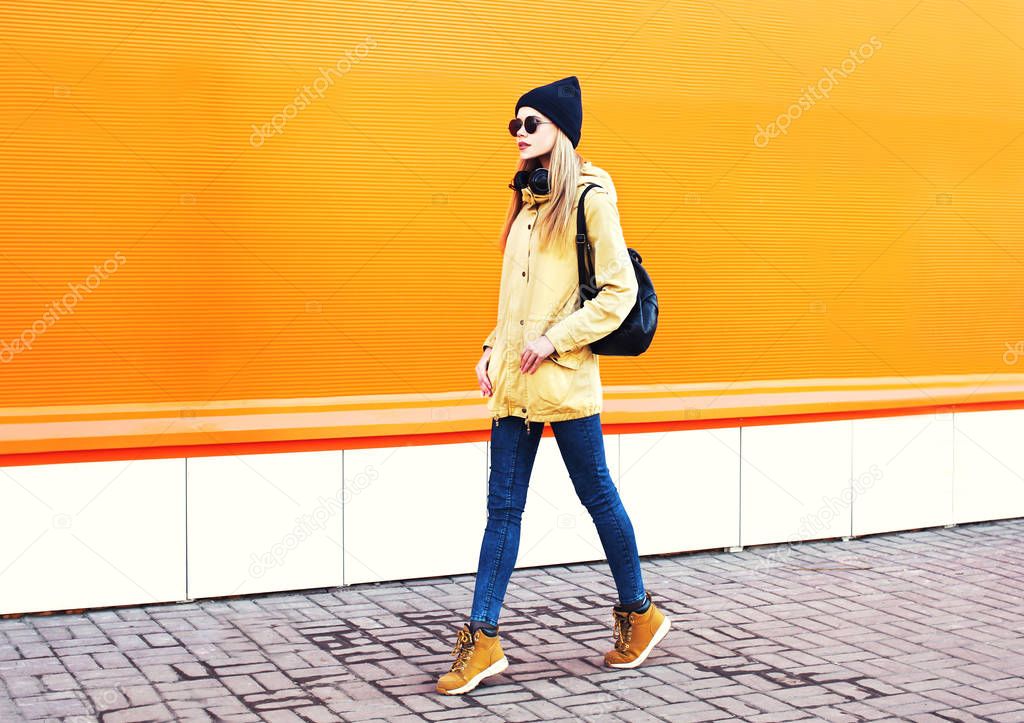 Fashion pretty blonde woman walking in city on a orange colorful