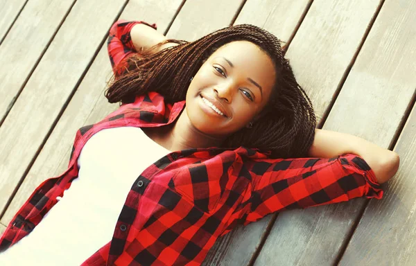 Retrato sorridente jovem mulher africana relaxado em um piso de madeira w — Fotografia de Stock