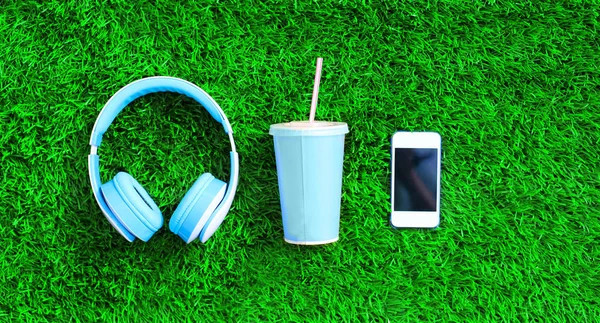 Kék fejhallgató, fehér smartphone, csésze gyümölcslé, egy zöld — Stock Fotó