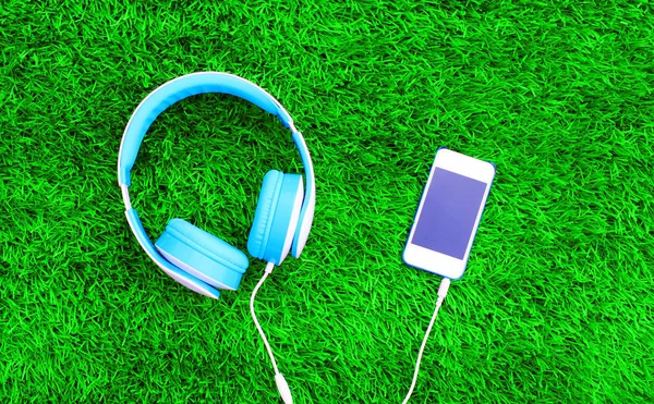 Fejhallgató van csatlakoztatva, a zöld fű textur fehér okostelefonok — Stock Fotó