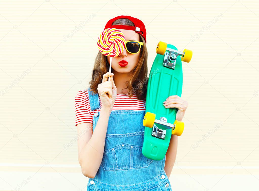 Fashion portrait of pretty cool girl with a lollipop and skatebo