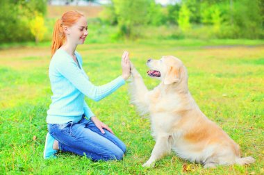 Mutlu sahibi kadınla çimenlerin üzerinde Golden Retriever köpek eğitiyor 