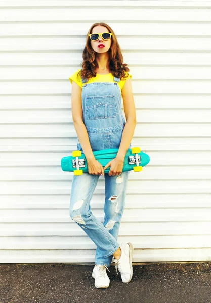 Bir kaykay üzerinde beyaz bir arka plan ile genç kadın moda