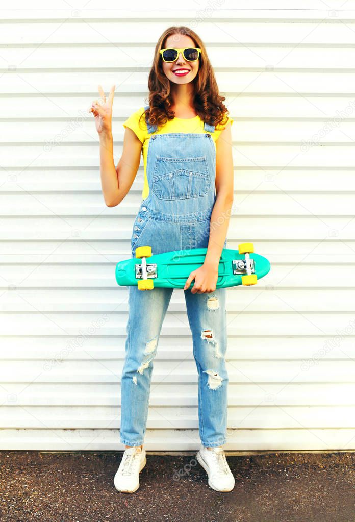 Fashion smiling young woman holds a skateboard having fun over a