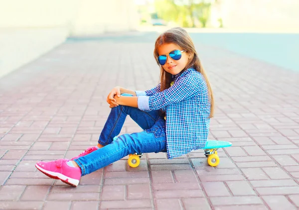 Enfant de mode petite fille assise sur le skateboard dans la ville — Photo