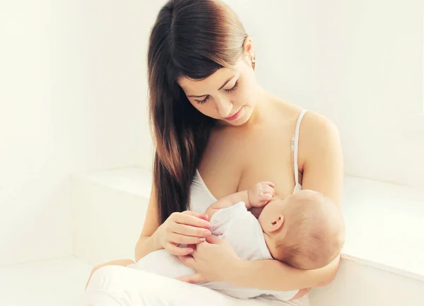 Mãe feliz alimentando o peito seu bebê em casa na sala branca — Fotografia de Stock