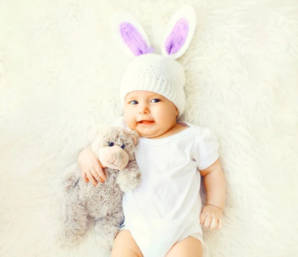 Joyeux bébé en bonnet tricoté avec des oreilles de lapin et un bea en peluche — Photo