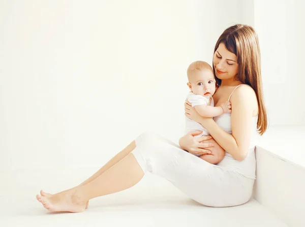 Feliz joven madre con bebé en casa en habitación blanca cerca de la ventana —  Fotos de Stock