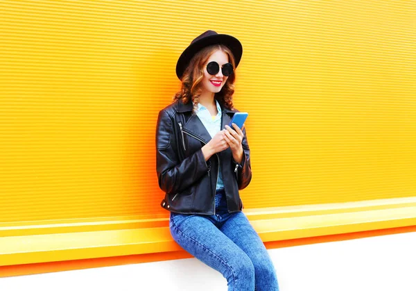 Fashion smiling woman is using smartphone in black rock jacket, — Stock Photo, Image