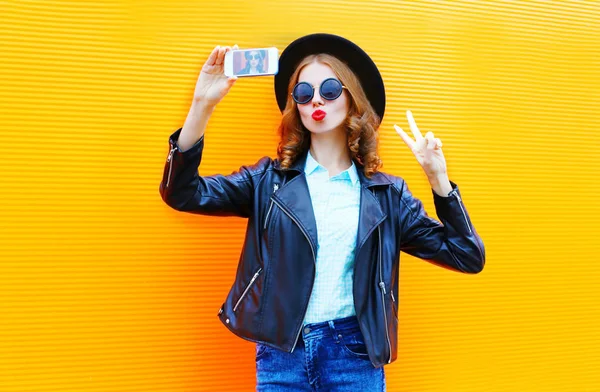 Mujer de moda está tomando una foto en un teléfono inteligente en el rock negro — Foto de Stock