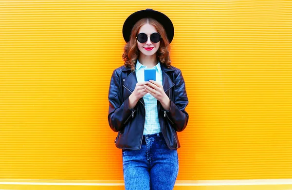 Fashion woman is using smartphone in black rock jacket on colorf — Stock Photo, Image