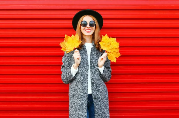 Moda otoño sonriente mujer con hojas de arce amarillo en un b rojo —  Fotos de Stock