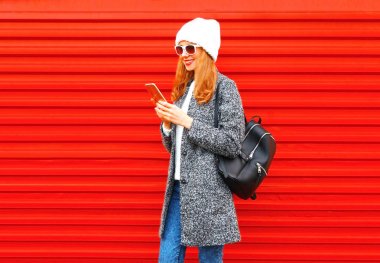 Şehir içinde kırmızı bir arka plan üzerinde akıllı telefon kullanan moda kadın