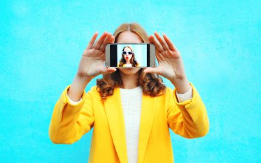 Kadın moda alır smartphone cep telefonu ile bir blu üzerinde kendi kendine portre resim