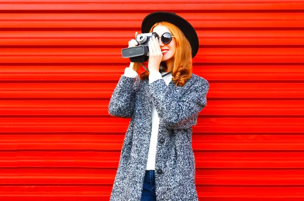 Retrato de moda mujer sonriente sostiene la cámara retro en un respaldo rojo — Foto de Stock
