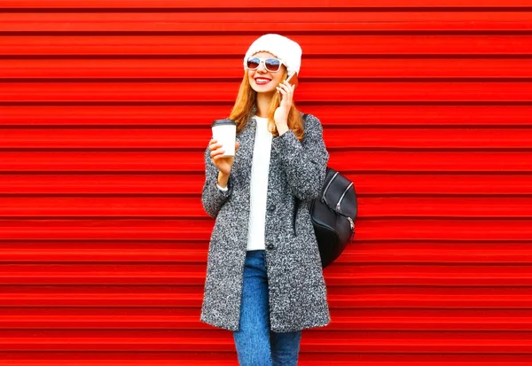 Moda sonriente mujer habla en un teléfono inteligente sostiene taza de café en — Foto de Stock