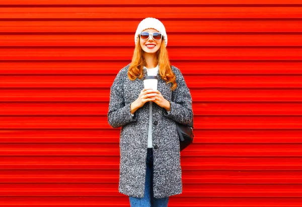 Модная улыбающаяся женщина с чашкой кофе в пальто на красном балахоне — стоковое фото