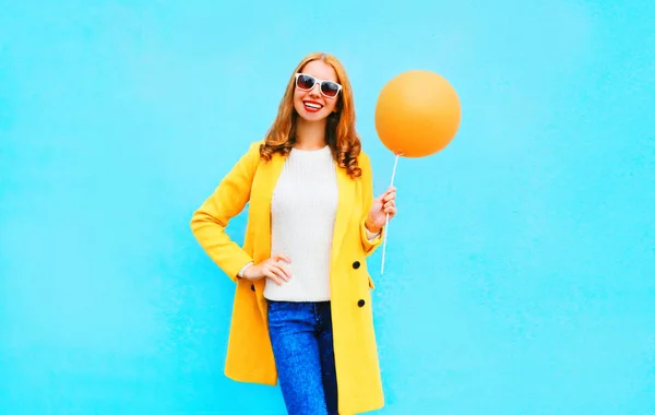 Модная улыбающаяся женщина держит воздушный шар в желтом пальто на blu — стоковое фото