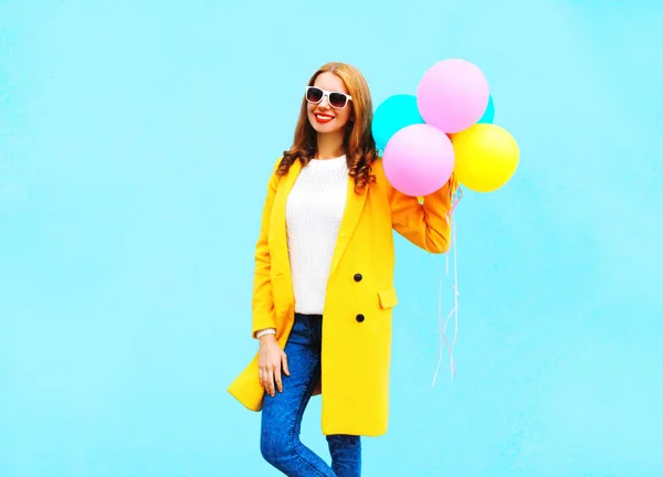 Mode lächelnde Frau mit Luftballons in gelbem Mantel auf einem b — Stockfoto