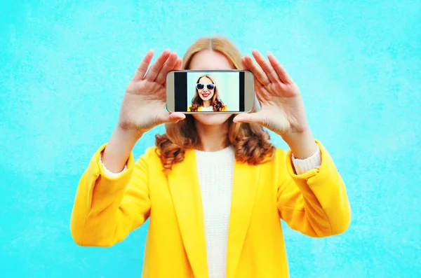 Mujer toma foto autorretrato en el teléfono inteligente en backgrou azul — Foto de Stock