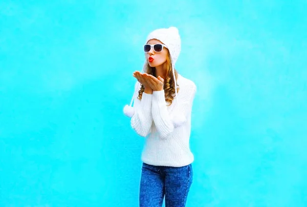 Mujer joven envía un beso de aire en suéter de punto, sombrero en un azul — Foto de Stock