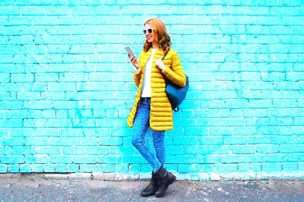 Moda jovem mulher usando smartphone em um fundo de tijolo azul — Fotografia de Stock
