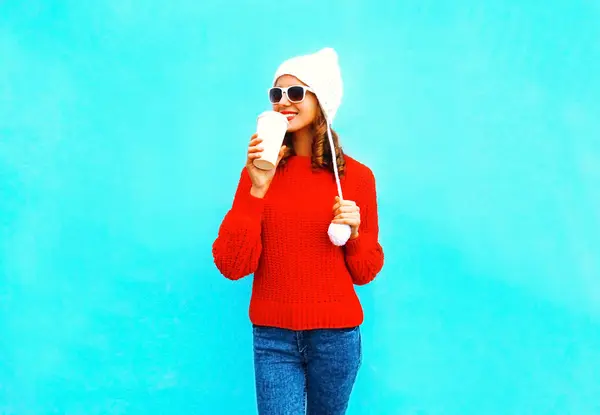 Donna felice beve caffè in maglione rosso, cappello su un backgrou blu — Foto Stock