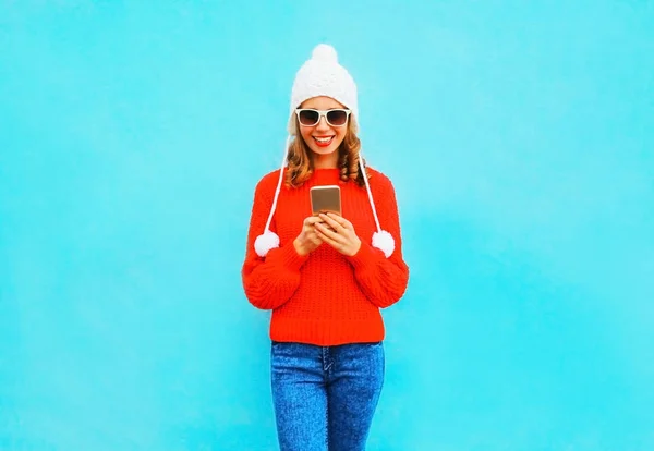 Mujer joven está utilizando el teléfono inteligente en suéter rojo, sombrero en una ba azul — Foto de Stock