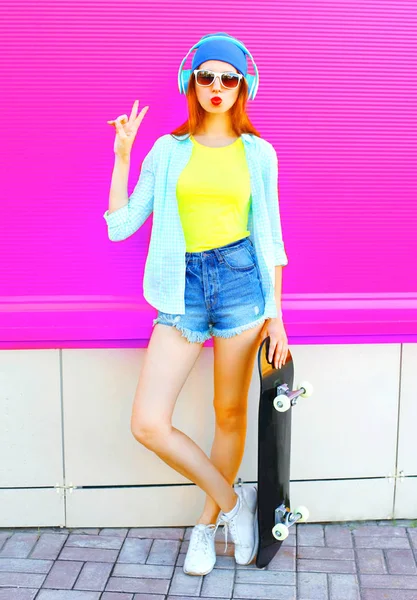 Fashion pretty woman listens to music with a skateboard on color — Stock Photo, Image