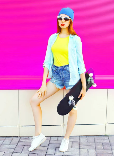 Mode ganska ung kvinna med en skateboard på rosa bakgrund — Stockfoto