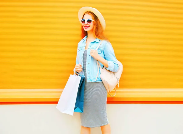 Mulher sorridente de moda com sacos de compras, chapéu de palha em uma laranja — Fotografia de Stock