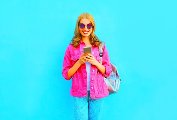 Moda mulher sorridente está usando smartphone em uma jaqueta de ganga rosa — Fotografia de Stock