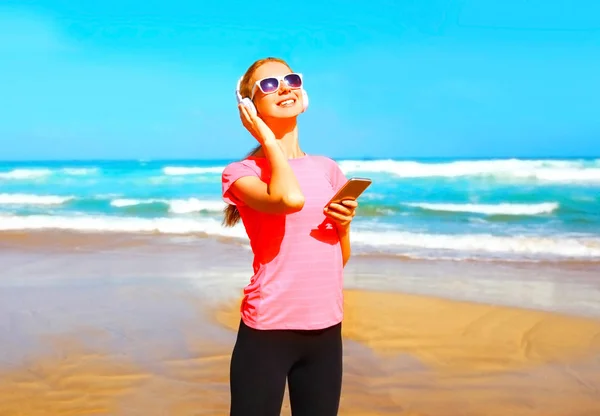 Fitness sorrindo mulher ouve música em um fone de ouvido sem fio — Fotografia de Stock