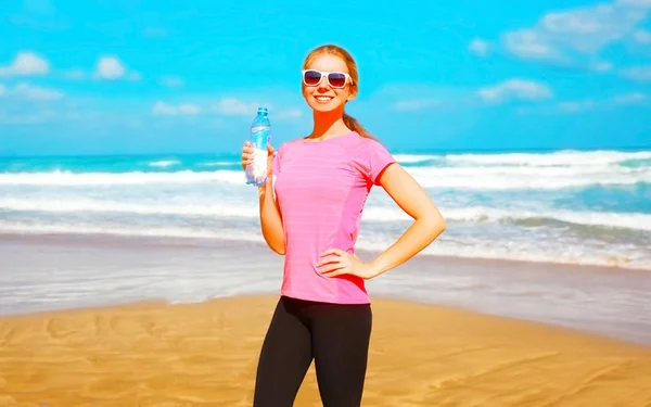 Mulher fitness com uma garrafa de água de plástico na praia perto do — Fotografia de Stock