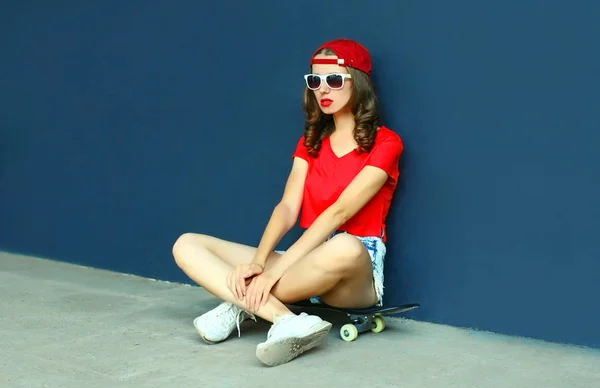 Junge Frau auf Skateboard sitzend, Baseballkappe, kurze Hose — Stockfoto