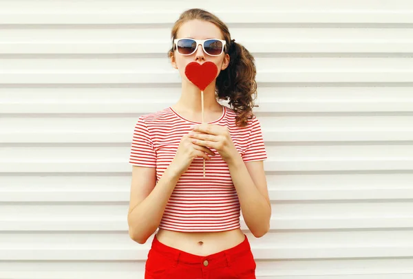 Beautiful young woman with red heart shaped sunglasses blowing l — Stock Photo, Image