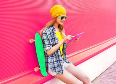 havalı genç bir kadın kaykaylı tablet kullanıyor. Renkli kıyafet giyiyor.