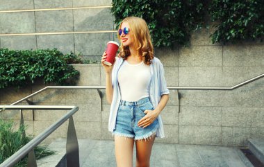 Elinde kahve fincanı olan güzel, gülümseyen genç bir kadın şehre bakıyor.