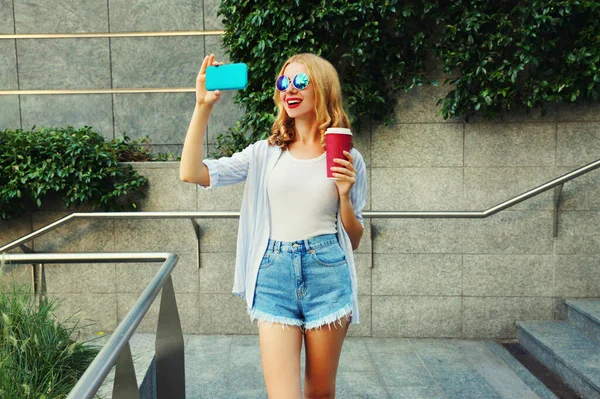 快乐的年轻女性在城市街道背景下 用智能手机与咖啡杯合影 — 图库照片