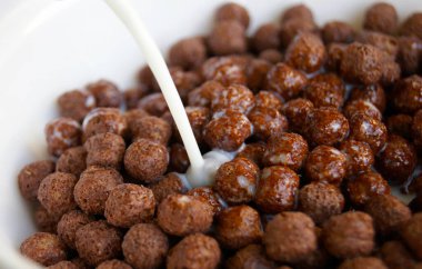 Kahvaltıda beyaz tabak ve çikolatalı mısır gevreği. Süt dök. Makro çekim.