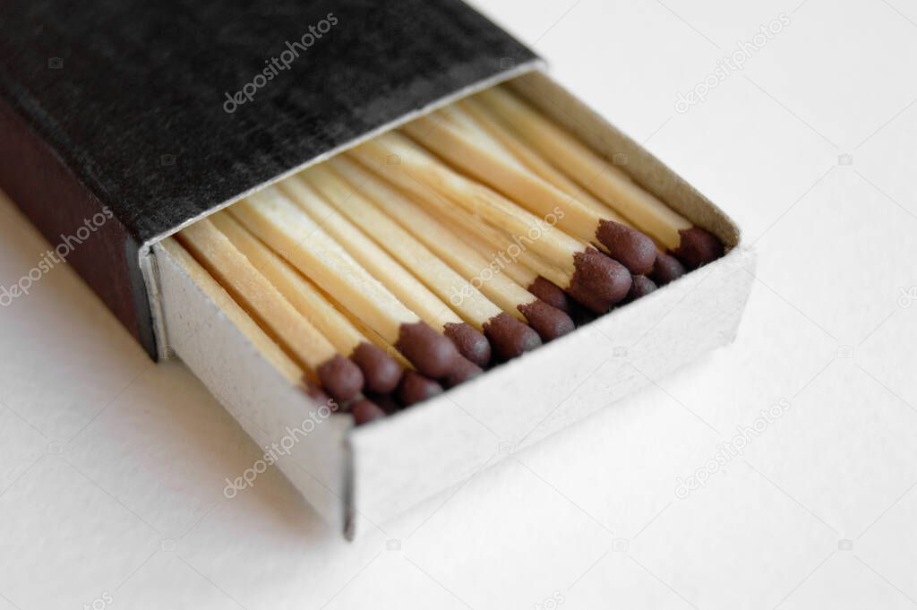 Long wooden safety matchsticks stacked in cardboard matchbox on white background.