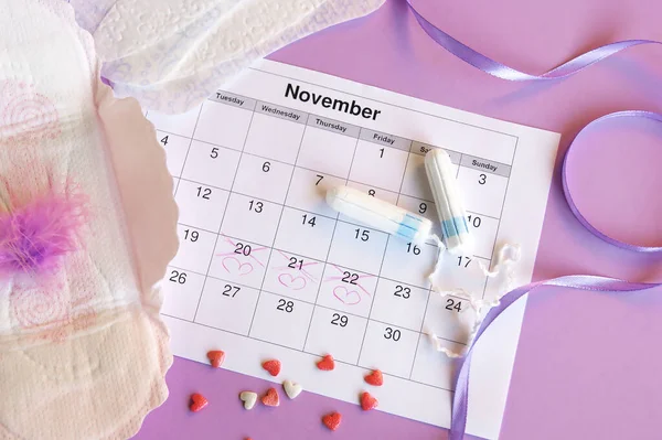 Menstrual pads and tampons on menstruation period calendar with on lilac background.