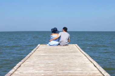 Sevgi dolu bir çift iskelede kucak kucağa oturuyor. Yaz. Aşk.